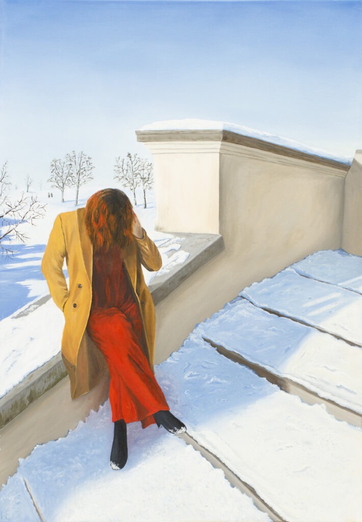 kim jestem - Ewelina Wasilewska - kobieta w beżowym płaszczu i czerwonych spodniach siedzi na ośnieżonym murku schodów, w tle zimowy krajobraz